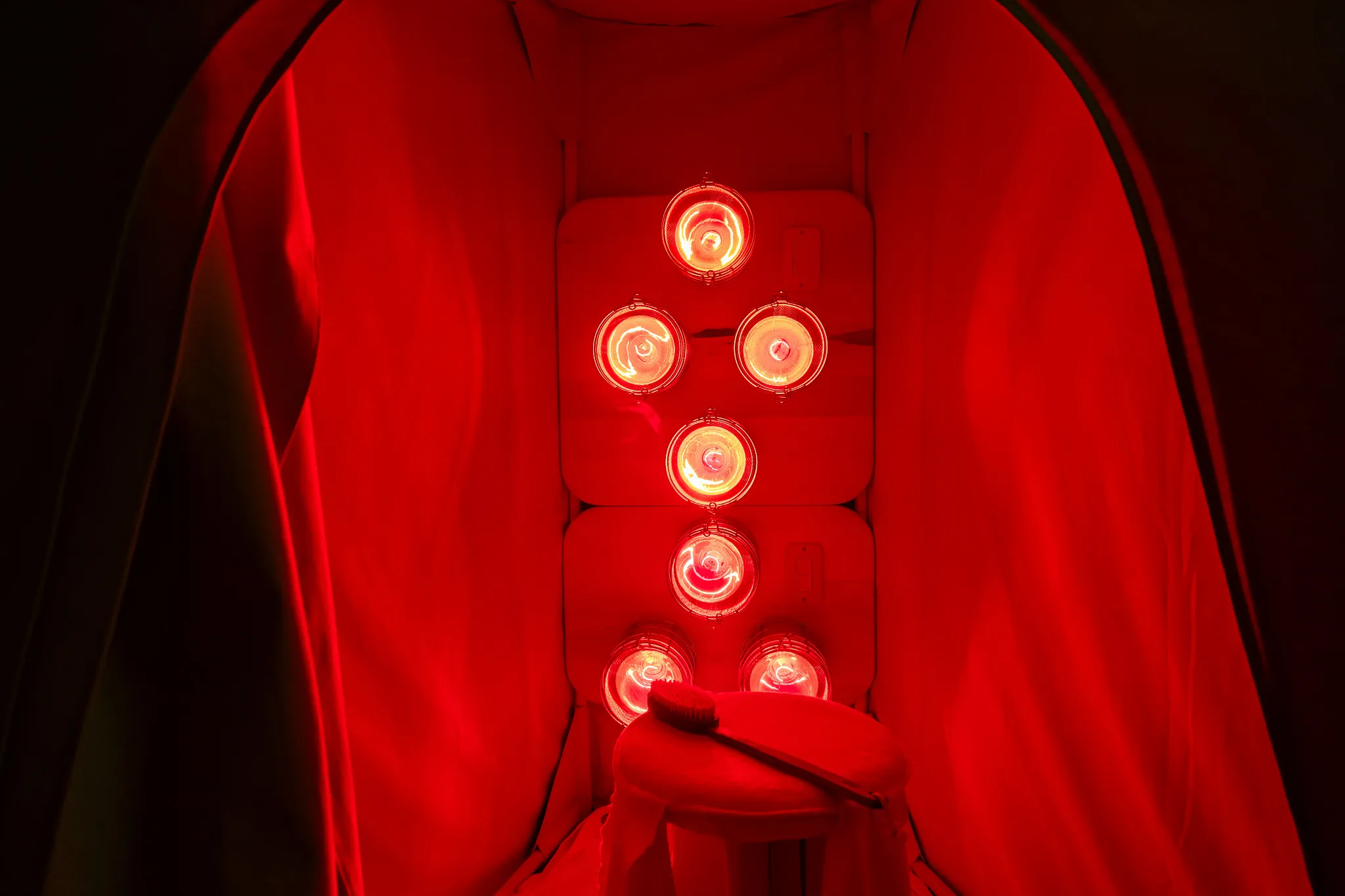 Interior of an infrared sauna with glowing red light therapy bulbs and a wooden body brush.