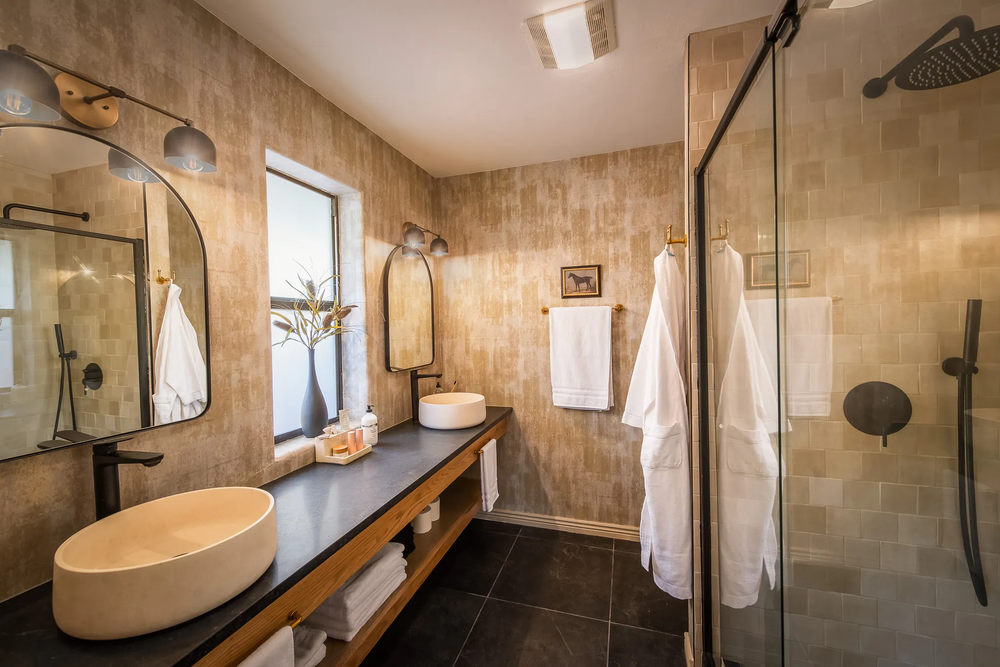 Designer bathroom with dual stone vessel sinks, arched mirrors, and a glass walk-in shower in a Sedona retreat.