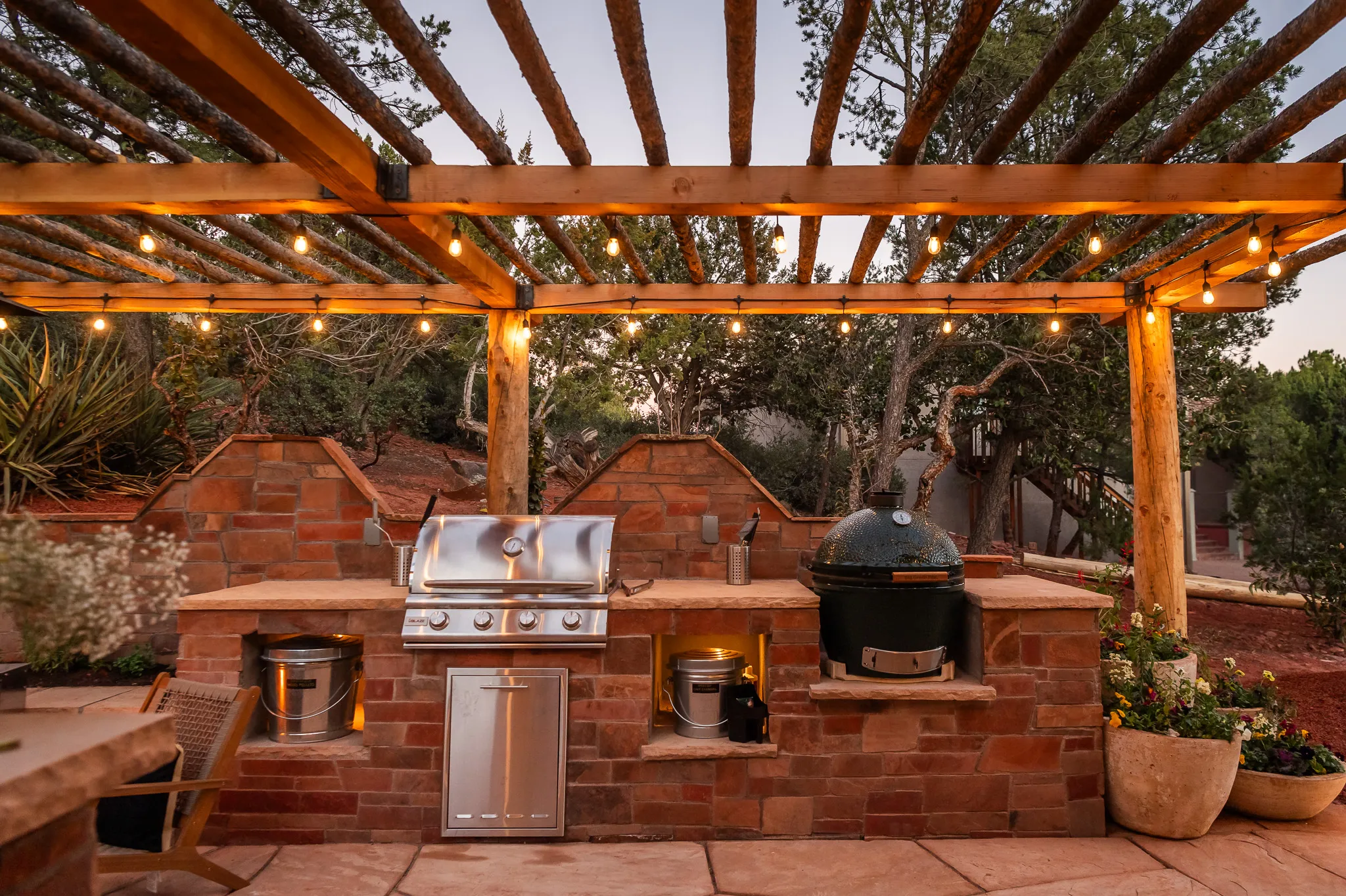 Outdoor kitchen with grill and smoker under a lit wood pergola at a Sedona luxury retreat.