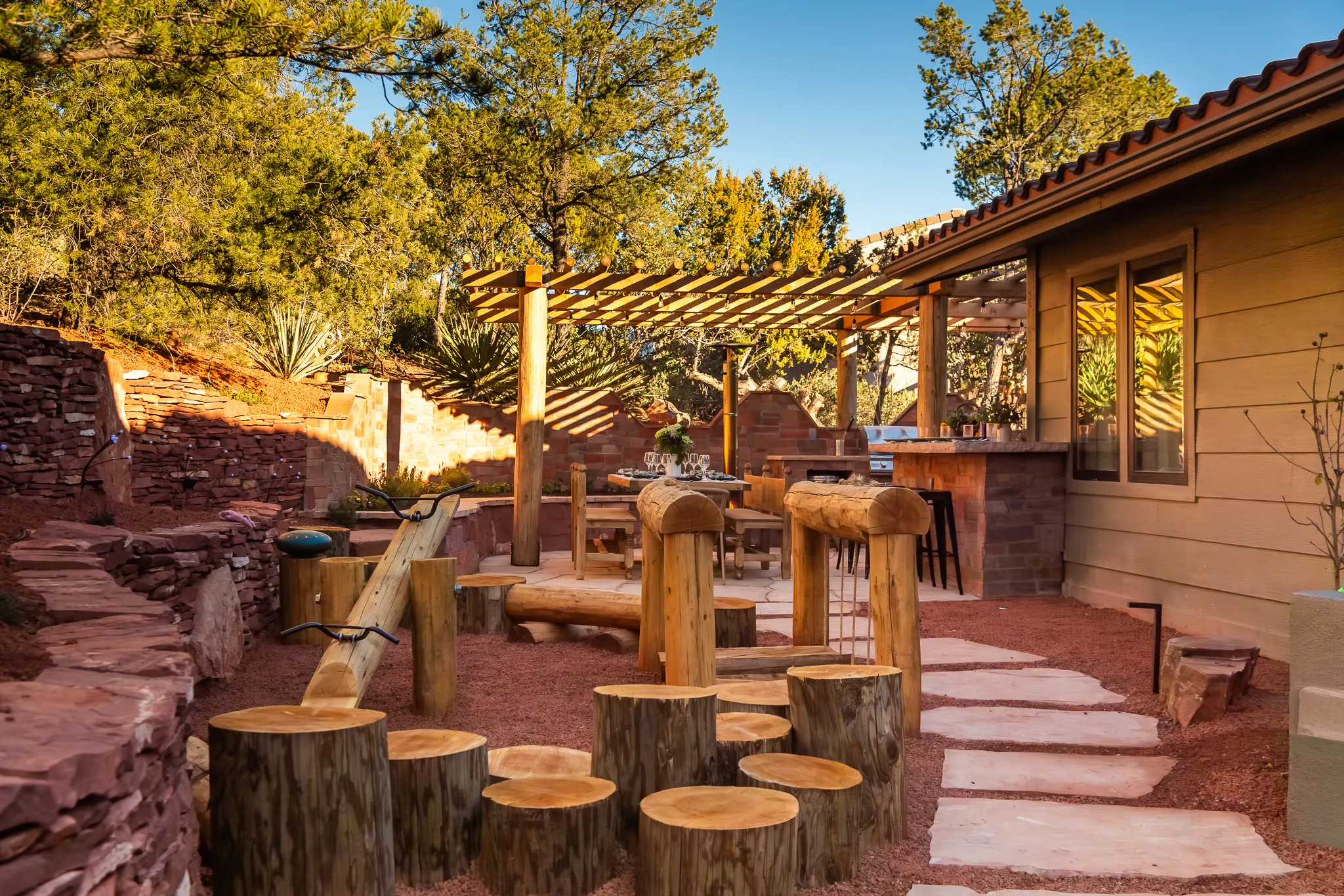 Natural log playground with tree stumps and see-saw near an outdoor kitchen in a West Sedona backyard.