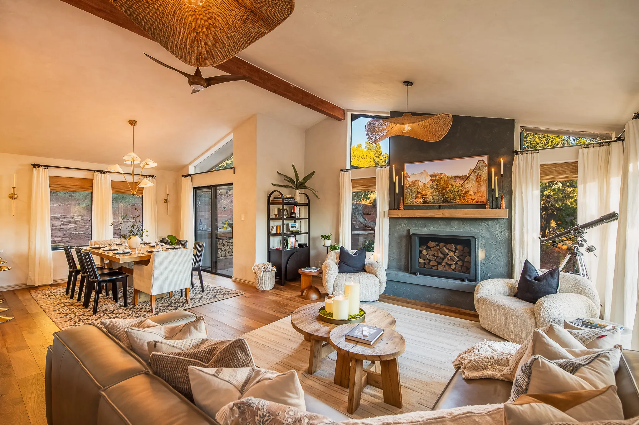 Modern living room with a stone fireplace, designer armchairs, and dining area featuring Sedona red rock views.