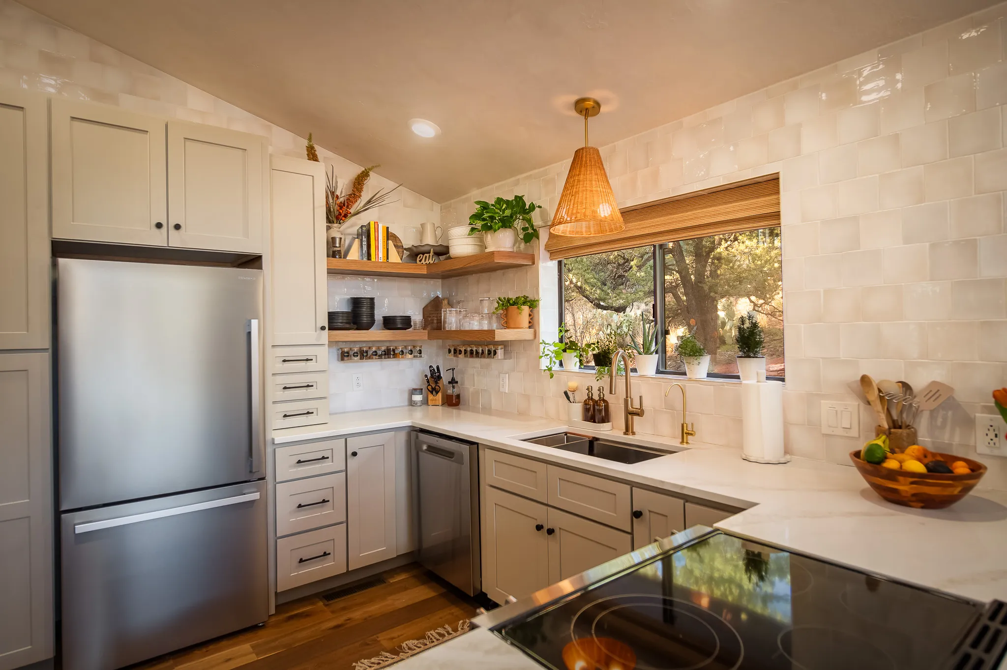 Modern kitchen with grey cabinets, open shelving, and lush tree views through the window in Sedona.