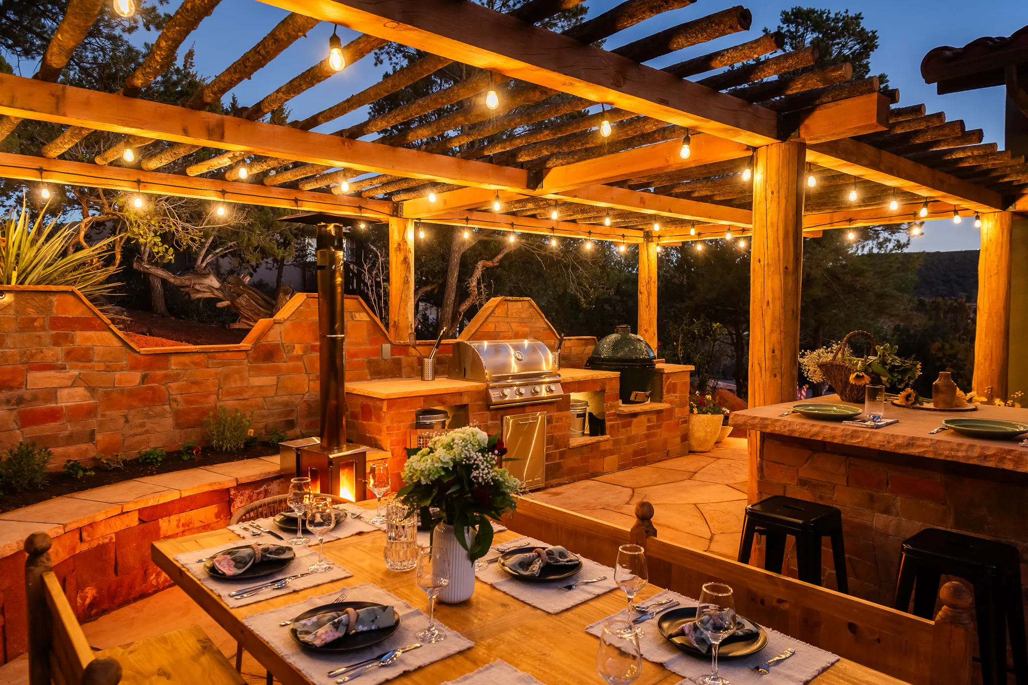 Gourmet outdoor kitchen with grill and smoker under a pergola with string lights at a Sedona retreat.