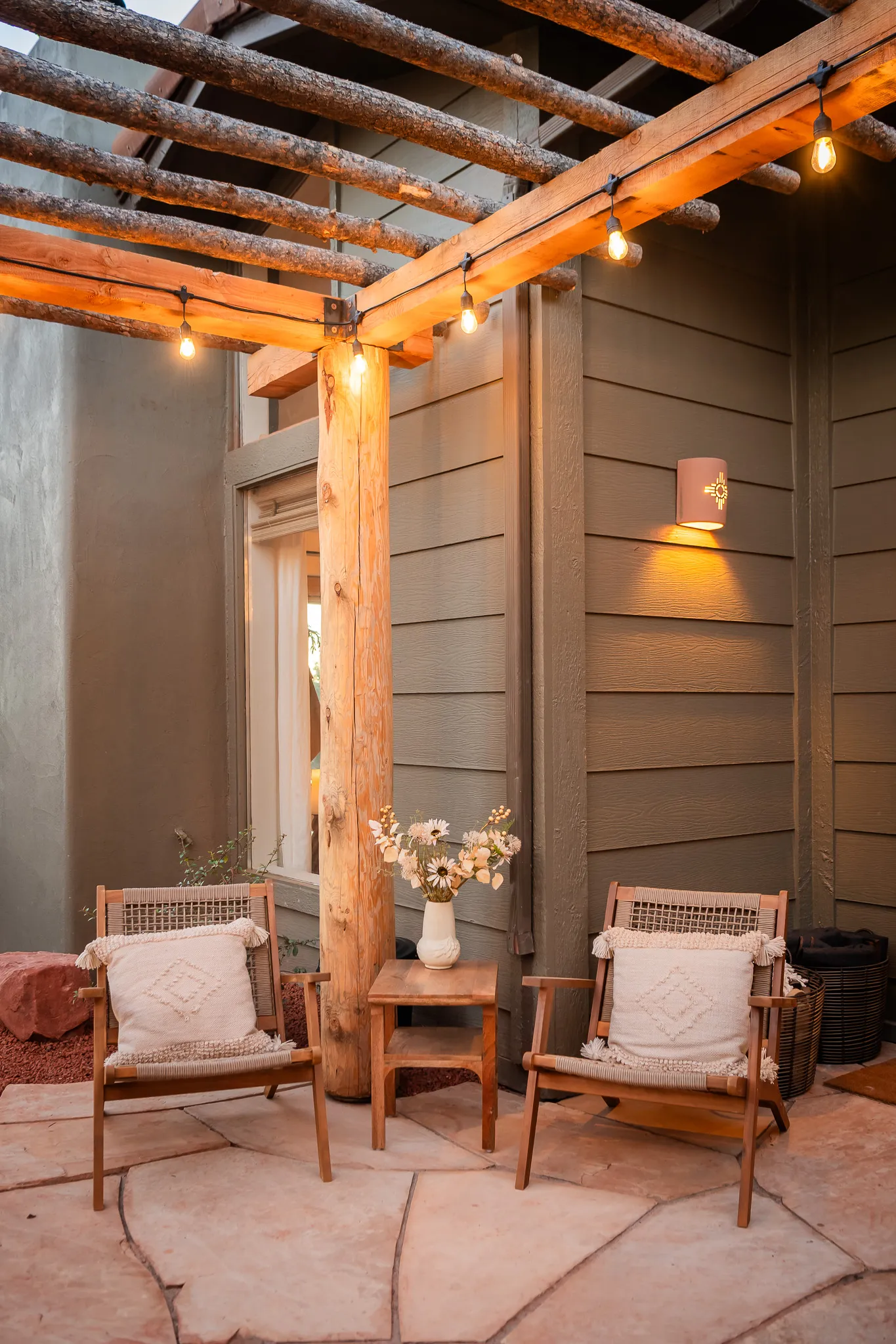 Two wooden lounge chairs under a lit pergola on a flagstone patio at a Sedona luxury retreat.