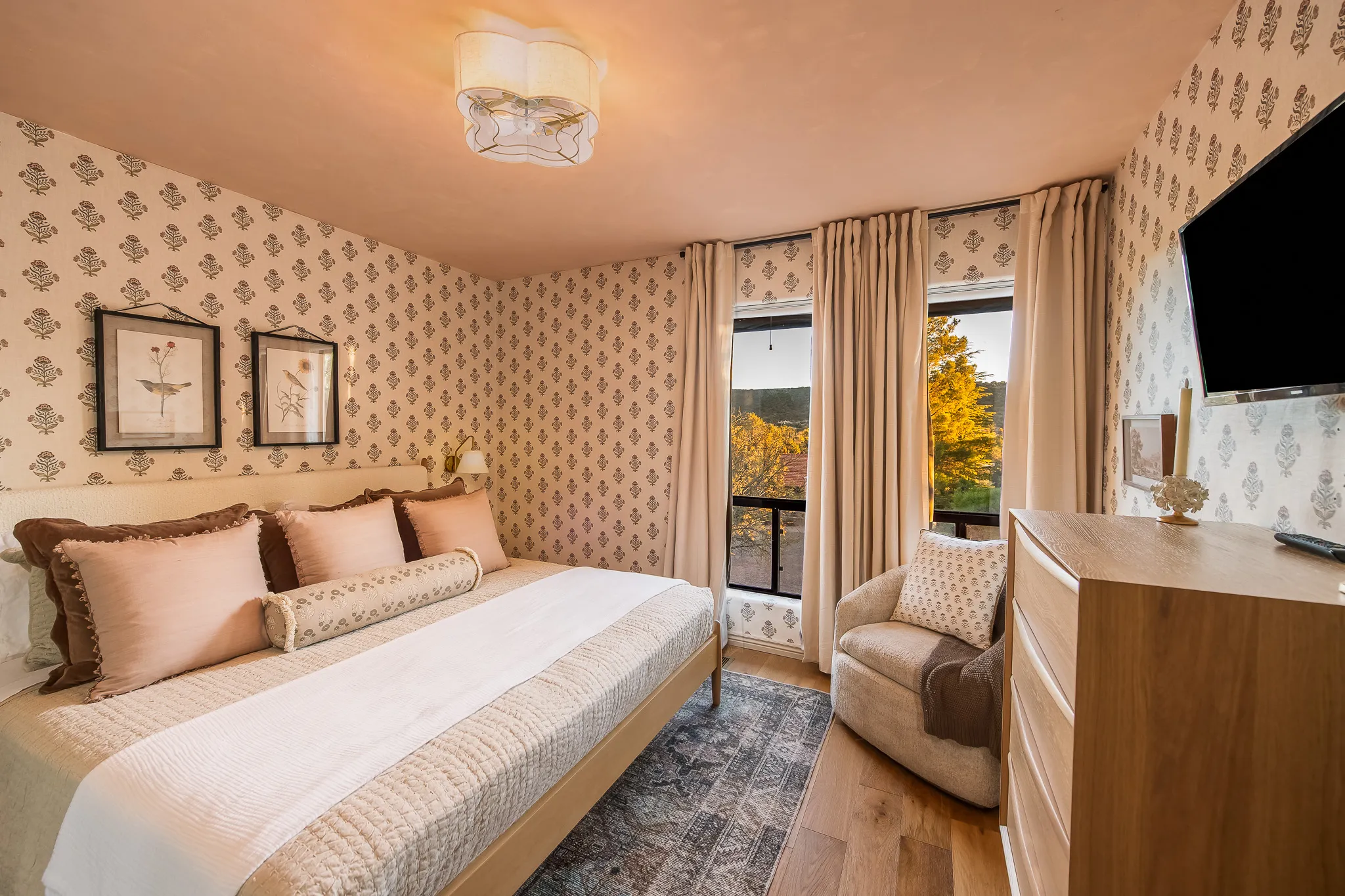 Floral wallpaper bedroom with organic linens, plush bed, and window view of Sedona trees at sunset.