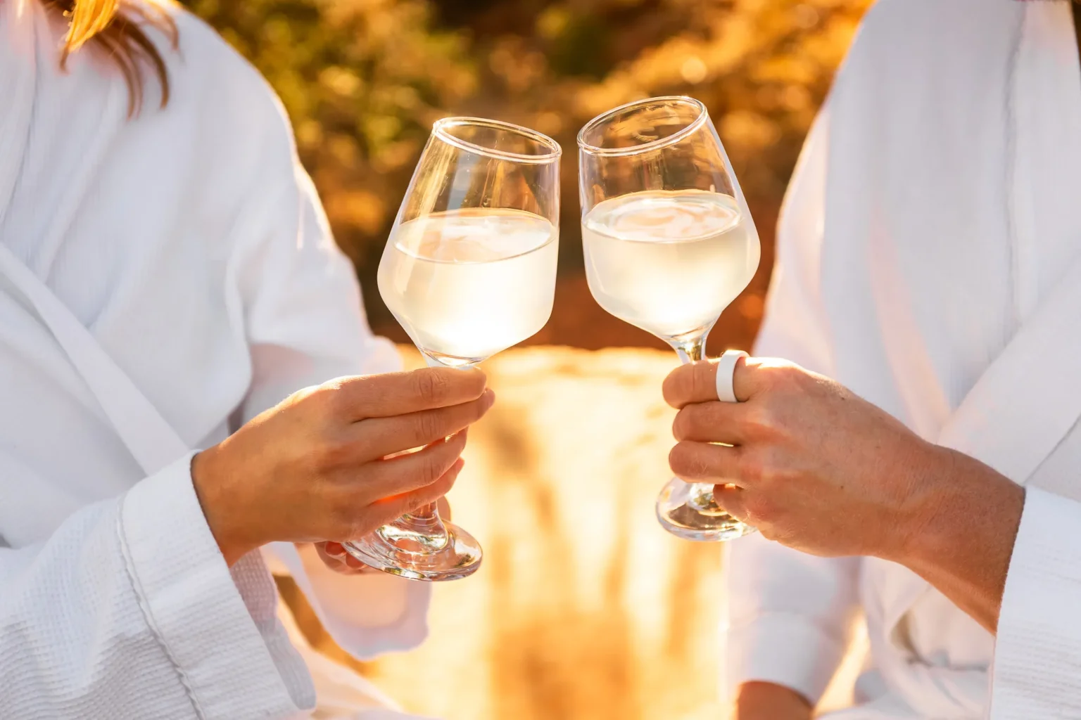Two people in white spa robes clinking glasses during sunset at a luxury Sedona wellness retreat.